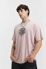 Remera de manga corta color rosa pálido con escote redondo y fit regular. Presenta un arte estampado en relieve en el centro del pecho con texto circular.