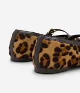 Zapatilla estilo Mary Jane de cuero con estampado animal print de leopardo. Presenta una tira superior ajustable con hebilla metálica dorada y detalles de ribete en color marrón oscuro.