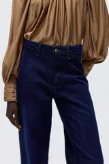 Pantalón de jean de tiro alto con corte recto y pierna ancha. Confeccionado en denim rígido, presenta cierre frontal con botón, bolsillos laterales, bolsillo monedero y bolsillos traseros.