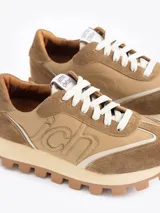 Zapatilla Mumi de cuero vacuno flor y descarne, color gris claro y celeste, con bordado "JCH" en el lateral. La base es de caucho para mayor liviandad y confort. Incluye cordón de algodón.