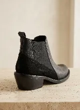 Bota tipo Chelsea de cuero negro con paneles laterales elásticos y taco bajo cuadrado. Presenta una combinación de texturas en el cuero y una presilla trasera para facilitar el calce.