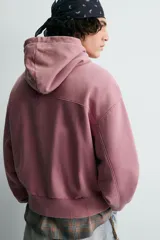 Sudadera tipo hoodie con cierre frontal de cremallera, diseño boxy fit, capucha ajustable con cordones, mangas largas con puños elásticos y bolsillos laterales. Presenta un acabado con efecto lavado.