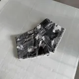 Short de denim estilo camuflado en tonos grises y negros, con diseño corto, dobladillo desmechado y detalle de estrella estampada en el bolsillo trasero.