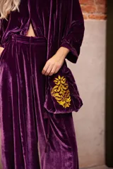 Cartera de mano tipo bolsa confeccionada en terciopelo de seda color violeta, con bordado floral en hilo dorado y detalle de borlas colgantes.