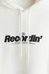 Canguro blanco de mezcla de algodón con interior cepillado suave y estampado frontal negro con la palabra "Recordin'". Tiene capucha de doble capa con cordón ajustable, hombros caídos, bolsillo canguro y puños y bajo acanalados. Corte holgado.