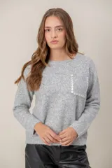 Sweater de punto gris con cuello redondo, manga larga y bolsillo frontal decorado con botones brillantes.