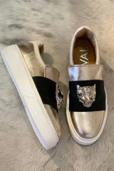 Panchas doradas con aplique de cuero negro y cabeza de tigre plateada.