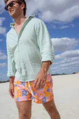 Short de baño corto con estampado de flores de colores sobre fondo rosa. Tiene cintura elástica con cordón ajustable y bolsillos laterales.