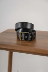 Cinturón de cuero negro con hebilla metálica en tono bronce envejecido y ojales reforzados.