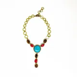 Collar corbatero de bronce con piedras naturales engarzadas. El diseño central presenta una piedra turquesa ovalada, flanqueada por piedras rojas y piedras ojo de tigre ovaladas. De esta piedra central cuelga una cascada de piedras rojas y ojo de tigre engarzadas en marcos de bronce.