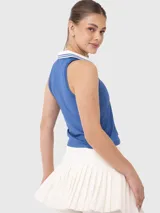 Conjunto deportivo compuesto por una musculosa azul con cuello polo y detalles en blanco, y una pollera short (skort) plisada de color blanco con cintura elástica.