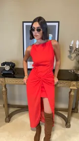 Vestido largo rojo con diseño asimétrico, escote redondo y detalle de nudo drapeado en la cintura que crea una abertura frontal, dejando ver una falda corta interior.