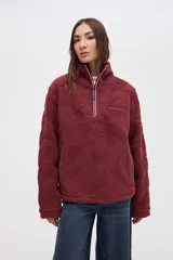 Buzo de sherpa con textura capitoneada, color bordó, con cuello alto y cierre frontal parcial. Presenta bolsillos laterales y calce relajado.