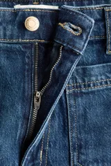 Jean de denim color azul oscuro, con corte wide leg de tiro alto, bolsillos delanteros de parche y pliegues marcados al frente.