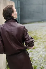 Pollera tubo de cuero sintético color marrón oscuro, de largo hasta la rodilla, con tajo frontal y cierre oculto en la parte trasera.