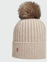 Gorro tipo beanie de punto acanalado en color beige, confeccionado en cachemir, con detalle de pompón superior y logo de la marca aplicado en el frente.