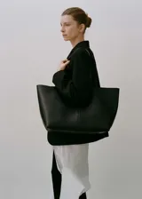 Bolso tipo shopper de cuero bovino, con diseño minimalista, costura central vertical y doble asa de hombro. Cuenta con cierre magnético y forro interior de cuero.