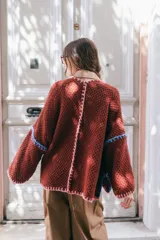 Saco oversize de tejido de punto en color beige, con mangas caídas y detalles de bordado a mano en tonos verde y lila en los bordes y costuras.