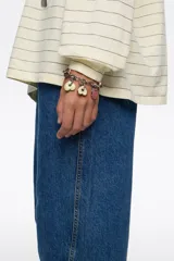 Pulsera de cadena metálica plateada con cierre de mosquetón. Presenta múltiples dijes colgantes en forma de corazón y discos circulares esmaltados en colores rosado, naranja, amarillo, verde y bordó, con el logo de la marca grabado en cada pieza.