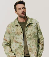 Campera trucker de Marfinno para hombre, con diseño de estampado floral en tejido jacquard texturizado de tonos verdes y beige. Presenta cuello camisero, cierre frontal de botones metálicos y bolsillos en el pecho.