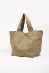 Bolso tipo shopper de color beige, con diseño amplio y doble asa de hombro. Presenta un detalle frontal de bordados coloridos con hilos colgantes que forman un diseño artístico.