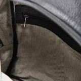 Mochila de cuero negro con textura granulada, cierre principal con doble tirador y bolsillo frontal con placa metálica plateada con logo XL.