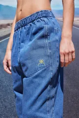 Pantalón de jean azul de corte babucha, tiro medio, con elástico en la cintura, bolsillos delanteros y logo bordado en amarillo en la pierna derecha.