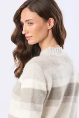 Buzo tejido de punto grueso con diseño de rayas horizontales en tonos rosado, beige y blanco. Presenta escote redondo, mangas largas y puños acanalados.