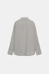Camisa fluida de corte oversize confeccionada en mezcla de viscosa, con diseño de rayas verticales finas en tono beige sobre fondo blanco. Presenta cuello solapa, cierre frontal con botones, manga larga con puños y un bolsillo de plastrón en el pecho.