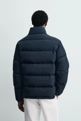 Campera puffer acolchada de corte regular fit, confeccionada en tejido técnico azul marino repelente al agua. Relleno interior de 80% plumón y 20% pluma. Cuenta con cuello subido, manga larga con puño elástico, bolsillos frontales de plastrón con solapa y cierre de cremallera oculta con solapa de botones a presión.