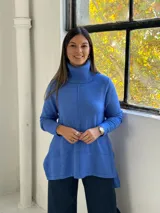 Sweater de punto color azul, con cuello alto acanalado, mangas largas y diseño holgado con costuras verticales decorativas.