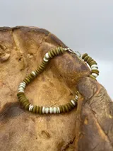 Pulsera de cuentas de madera color verde oliva y cuentas blancas, con cierre de gancho plateado.