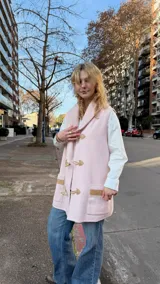 Chaleco de lana merino color rosa pastel, con cuello tejido tipo chal, cierre frontal con botones tipo duffle y bolsillos laterales con detalle en tono contrastante.