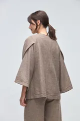 Capa de lana fina sin teñir, con diseño de corte amplio y mangas tipo kimono. Presenta cierre frontal mediante tres alamares de cuero en tono marrón.
