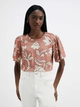 Blusa color salmón con estampado de flores blancas, de mangas cortas con volados y cuello redondo.