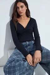 Top de manga larga color negro con escote en V y detalle de frunce central. Presenta un corte entallado que se adapta a la figura.