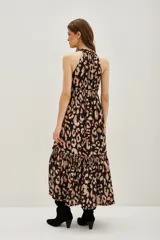 Vestido largo con estampado de leopardo en tonos negro y beige. Presenta cuello alto con detalle de frunce, tirantes anchos y cintura fruncida con elástico. La falda es larga con un volante en el ruedo.