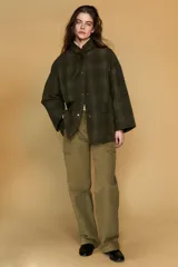 Chaqueta de algodón encerado con diseño de cuadros en tonos verde oliva, beige y líneas rojas. Presenta cuello solapa, cierre frontal con botones a presión metálicos, bolsillos de plastrón con solapa y un detalle de pañuelo desmontable sobre los hombros.