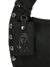 Cartera hobo de cuero sintético negro de la marca Hush Puppies, modelo Taffy. Presenta un diseño suave con una correa ancha para el hombro y detalles de tachas metálicas redondas a lo largo de los bordes laterales e inferiores. Incluye un llavero colgante con la silueta del perro basset hound característico de la marca y el logo impreso en la parte frontal.