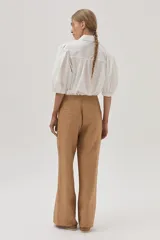 Camisa blanca de mangas abullonadas con puños elásticos, cuello clásico y cierre frontal con botones. Presenta detalles de bordado calado en el pecho.