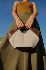 Bolso mini shopper de lona en color crudo con detalles en cuero sintético marrón en los laterales y una manija corta trenzada de mano. Cuenta con costuras contrastantes y cierre magnético.
