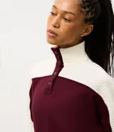 Buzo deportivo de corte oversized, con diseño bicolor en bordó y blanco. Presenta cuello alto con cierre de botones a presión, mangas largas con textura acanalada y puños elásticos.