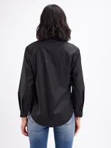 Camisa blanca de manga larga con cuello camisero, cierre frontal con botones y detalles de tablas verticales en el frente.