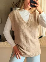 Chaleco tejido de punto en color beige, con escote en V y terminaciones acanaladas en cuello, sisas y ruedo.