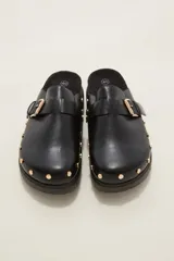 Suecos negros de estilo zueco con capellada de cuero sintético, detalle de hebilla metálica dorada y tachas decorativas alrededor de la suela. Poseen plantilla ergonómica y suela de plataforma dentada.