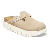 Zueco tipo mule de gamuza color beige, con diseño de punta cerrada, correa ajustable con hebilla metálica y suela de plataforma dentada en color blanco.