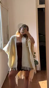 Ruana tejida artesanalmente en telar, color crema o blanco roto, con textura tejida y flecos en los bordes.