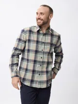 Camisa de manga larga confeccionada en tela de franela con estampado de cuadros en tonos beige, verde y azul marino. Presenta cuello clásico, cierre frontal con botones y un bolsillo en el pecho.