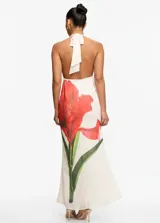 Vestido largo de fiesta color blanco con estampado floral de amapolas rojas. Presenta un escote halter con cuello drapeado, espalda descubierta y una silueta fluida y elegante.