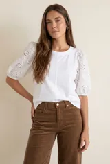Remera blanca de algodón con cuerpo liso y mangas globo de broderie con diseño floral calado. Presenta cuello redondo y costura central vertical en el frente.